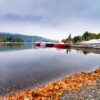 Landscape image of Lake Windermere in Lake District, a National Park in England, during Autumn with grey sky, autumn leaves and colourful boats next to jetty